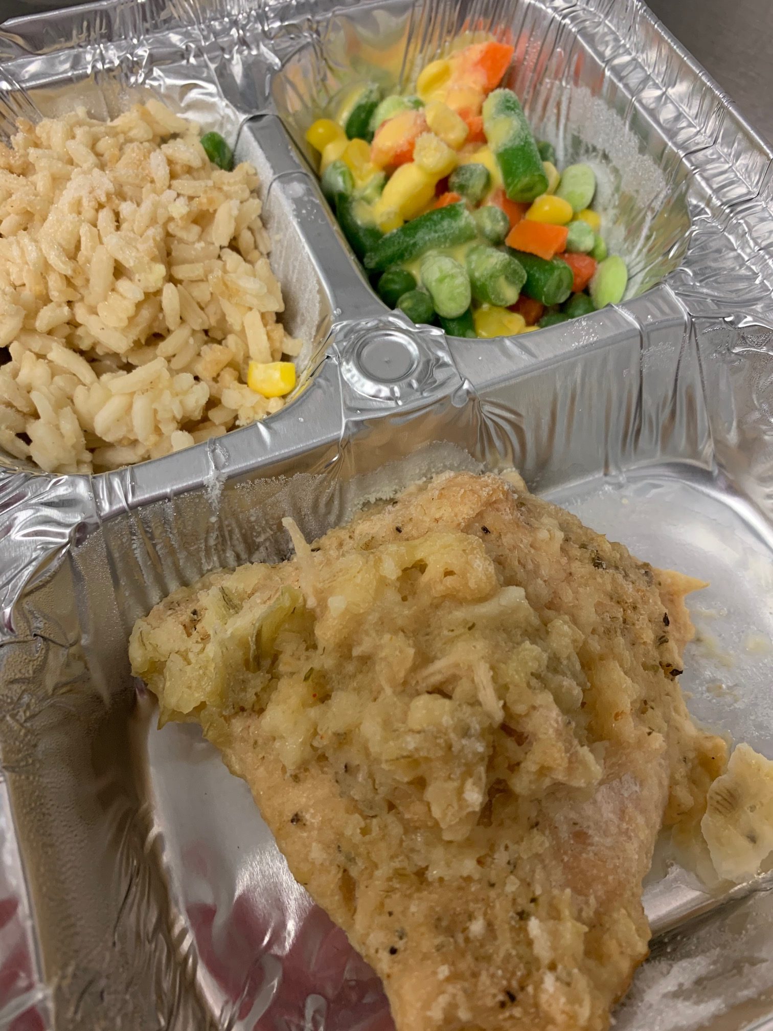 A frozen dinner of chicken, rice, and vegetables is shown packaged, frozen, and ready for delivery. Frozen meals are packaged with instructions for heating included directly on the lid. Meals are best reheated using a conventional oven.